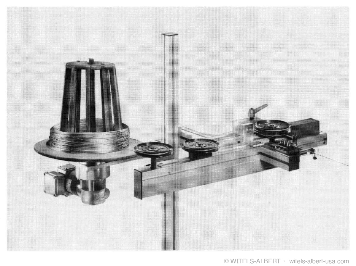 Photograph of a coiler unit with a cone-shaped wire pay-off, guide pulleys, and a small straightening unit mounted on a horizontal rail.