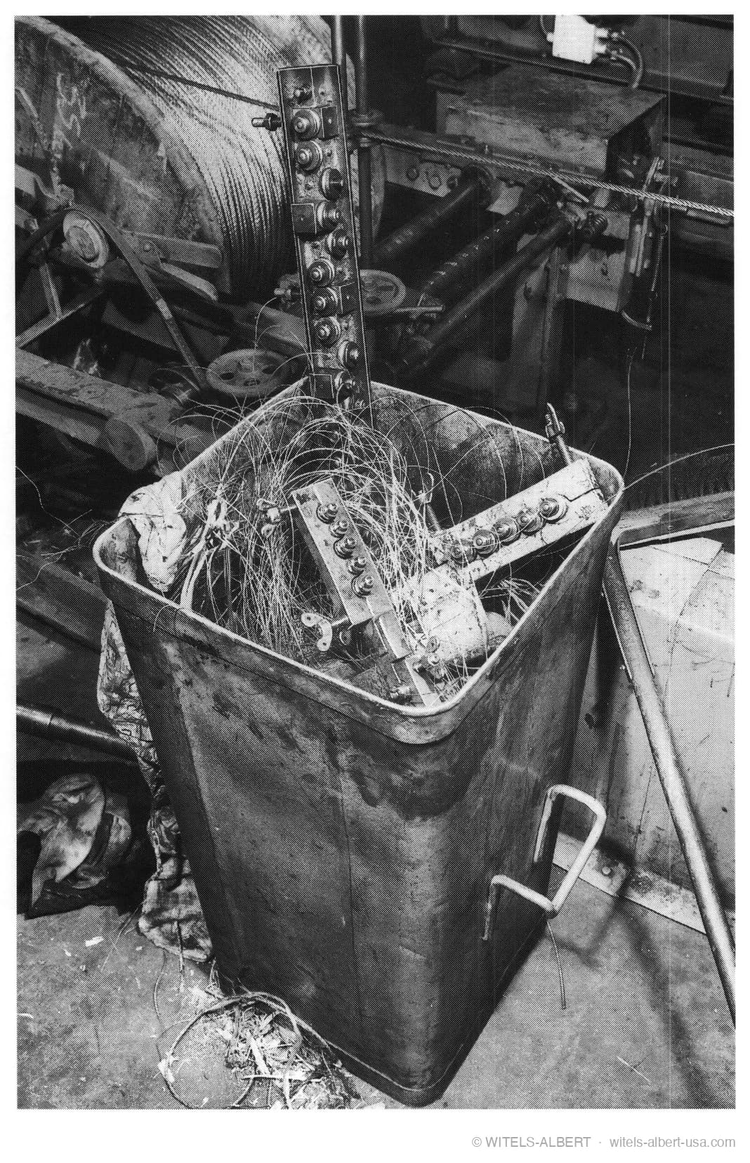 Photograph of a scrap bin overflowing with tangled, discarded wire next to a straightening unit on the shop floor of a wire mill.