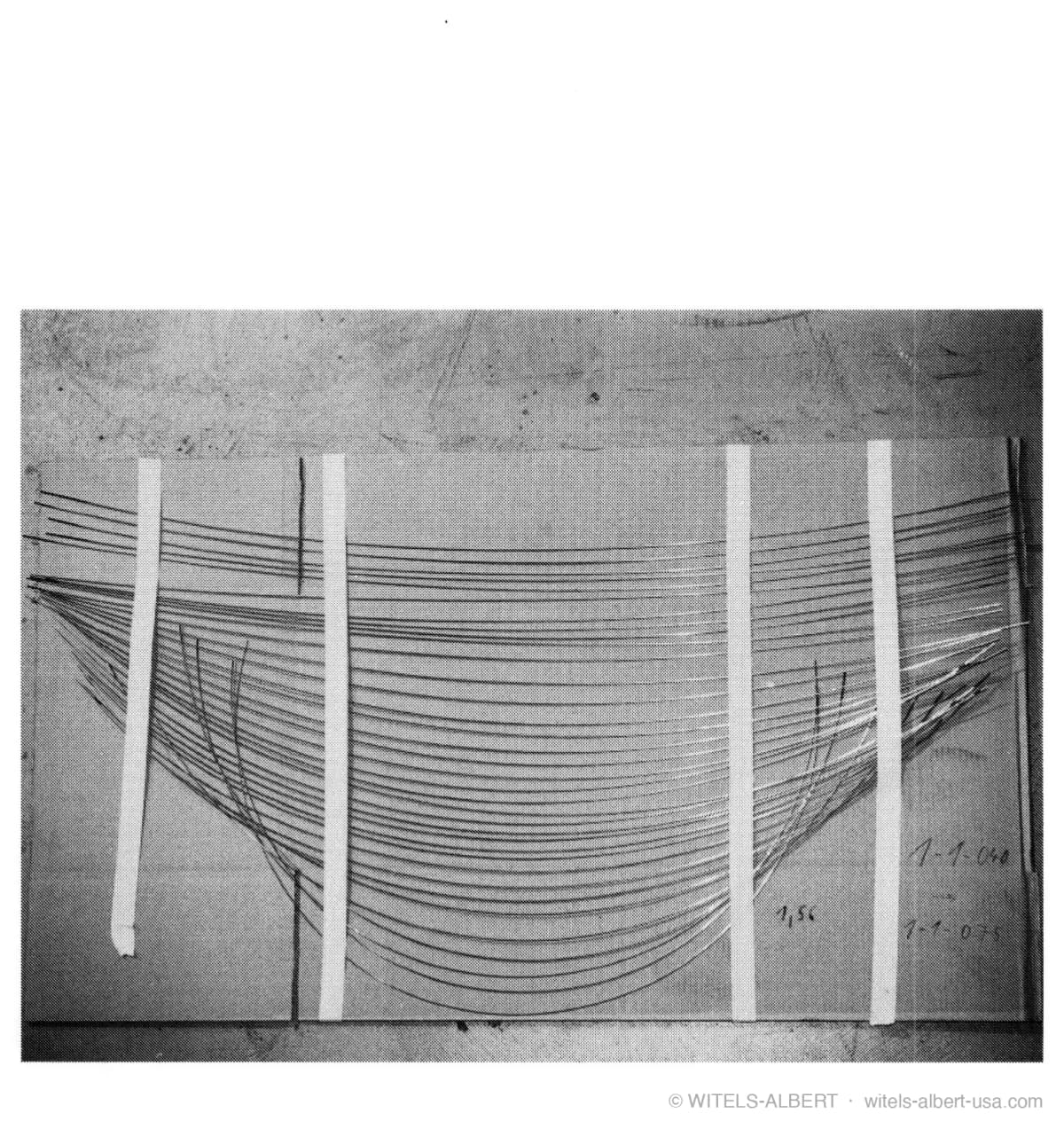 Photograph of many wire samples taped to a board, fanning out from a common origin to show a wide range of curvatures.