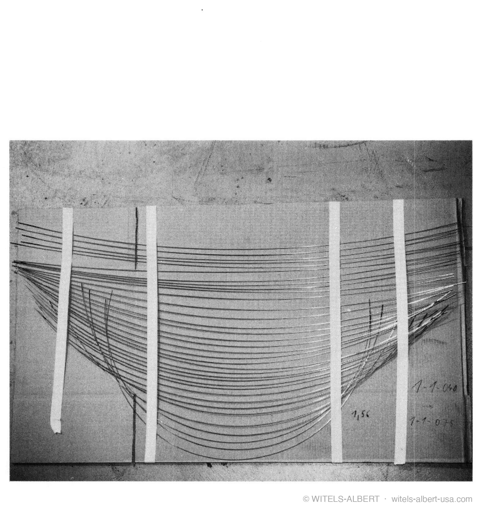 Photograph of many wire samples taped to a board, fanning out from a common origin to show a wide range of curvatures.