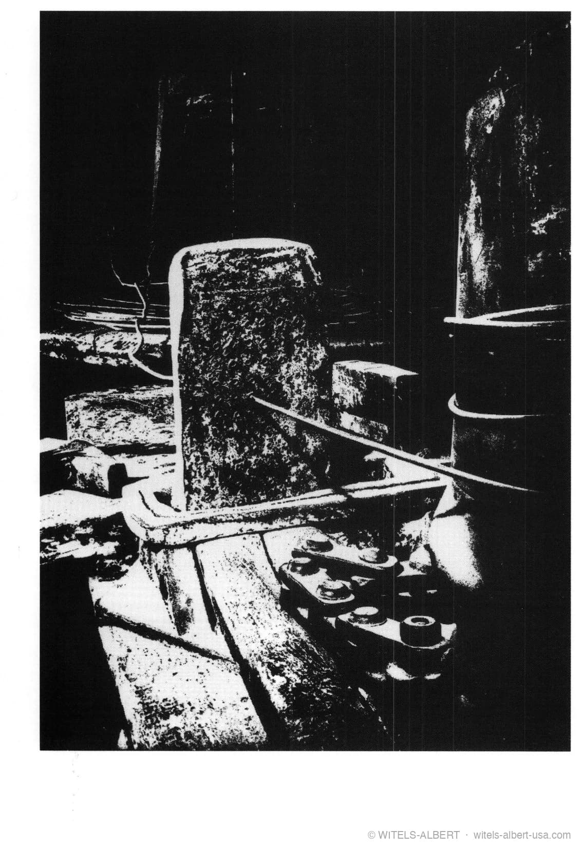 High-contrast photograph of a historical wire-drawing workplace with a heavy forged drawing iron and tools.