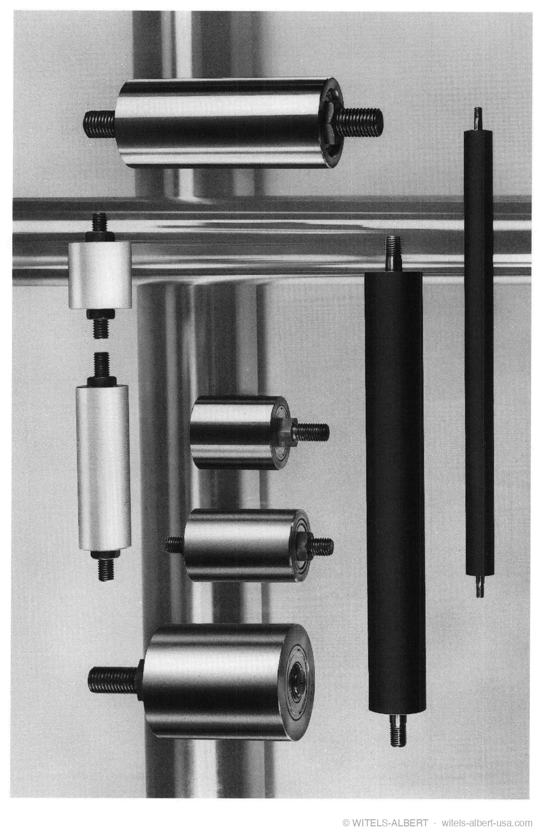 Product photograph of an assortment of cylindrical guide rolls in various diameters, lengths and materials, each with a threaded mounting stud.