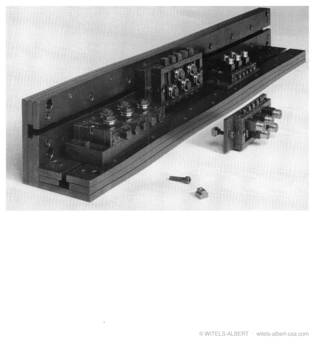 Photograph of a postforming apparatus: a long rail carrying adjustable roll blocks, shown with a detached roll module and fastening hardware.