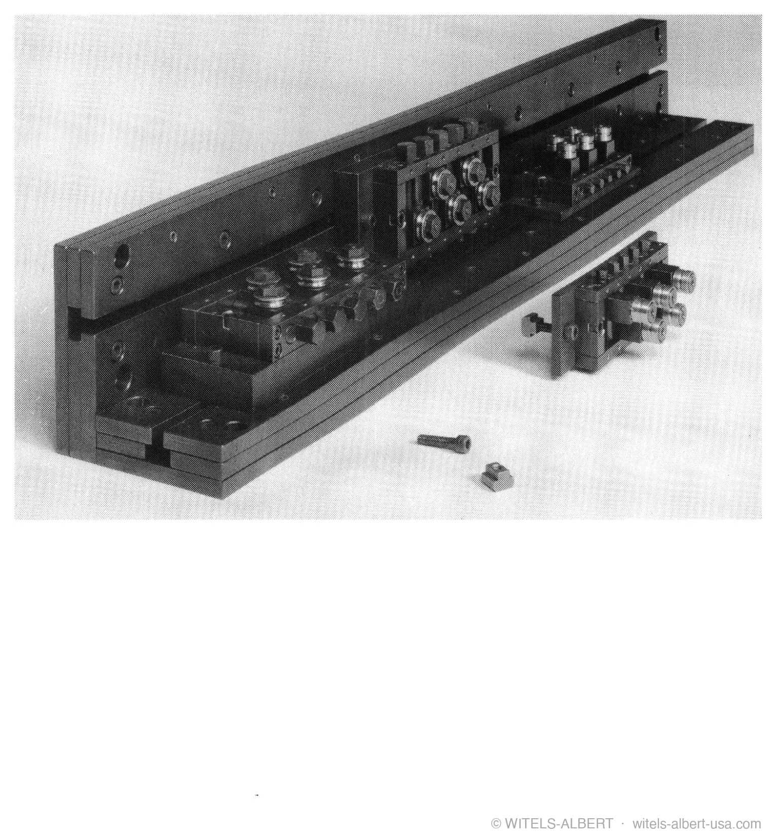 Photograph of a postforming apparatus: a long rail carrying adjustable roll blocks, shown with a detached roll module and fastening hardware.