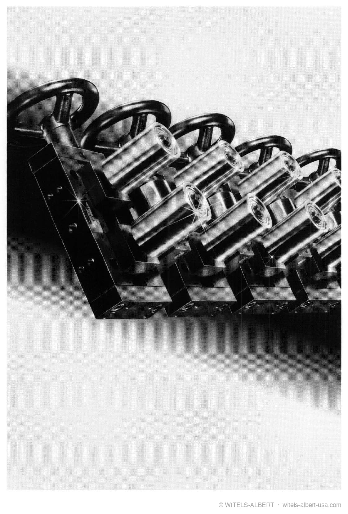 Photograph of a row of roller cross/guide units with polished cylindrical guide rolls and black handwheel adjusters mounted on a common rail.
