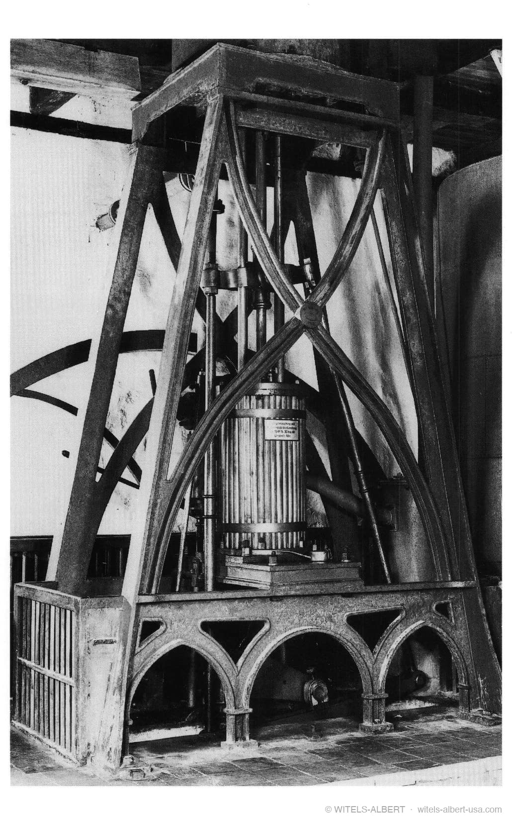 Photograph of a historical stationary steam engine with a tall cast-iron frame of Gothic arches surrounding a central vertical cylinder.